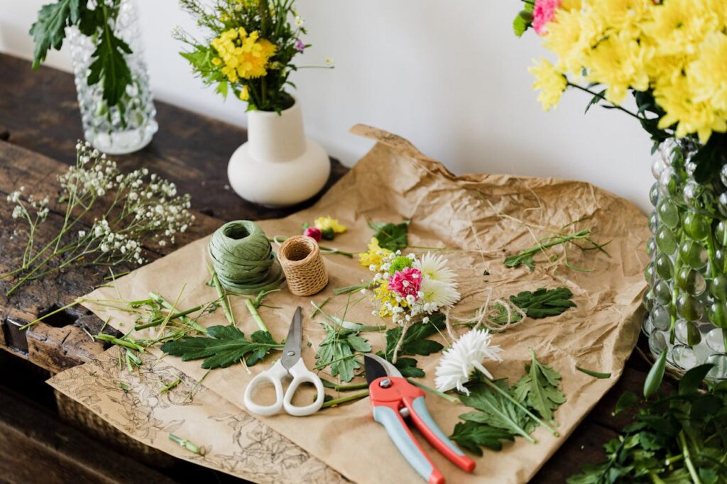 pexels-photo-4466584 Scissors and pruner on craft paper covered with cut leaves and flowers among bouquets on wooden table in floristry workshop